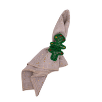Christmas Tree Napkin Ring, green woven crochet tree shape with red & yellow details, holding a beige linen napkin with metallic gold dots.