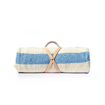 Beach Blanket Role, a rolled textured woven cotton blanket with cream and light blue stripes, secured by a tan leather carrier.