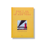 Don't Be a Tourist in New York by Vanessa Grall, golden yellow hardcover book with subtle textured pattern, featuring a red lighthouse and bridge, sta