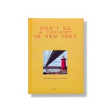 Don't Be a Tourist in New York by Vanessa Grall, golden yellow hardcover book with subtle textured pattern, featuring a red lighthouse and bridge, sta