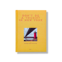 Don't Be a Tourist in New York by Vanessa Grall, golden yellow hardcover book with subtle textured pattern, featuring a red lighthouse and bridge, sta